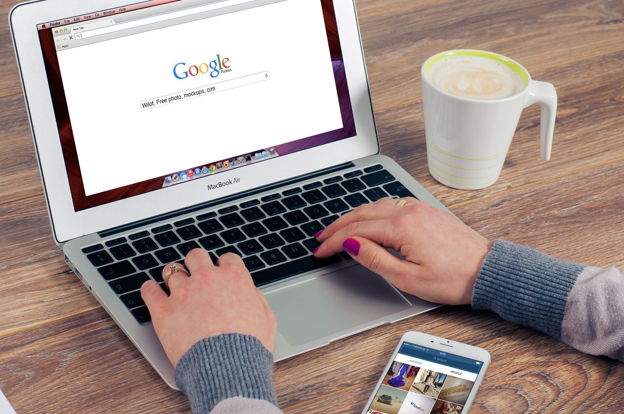 Fingers typing on a MacBook Air with Google search open, with coffee nearby.